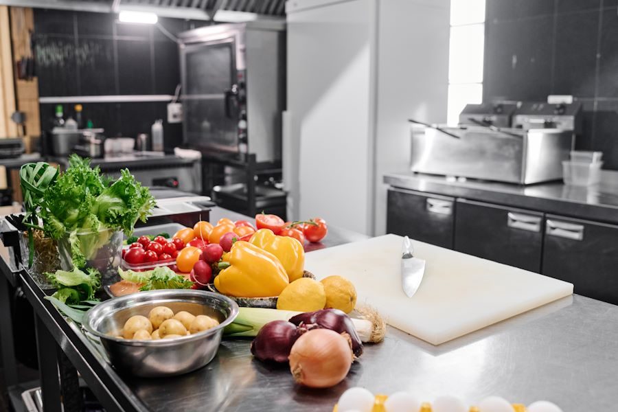 Image of workplace of chef with cutting board and fresh vegetables in commercial kitchen